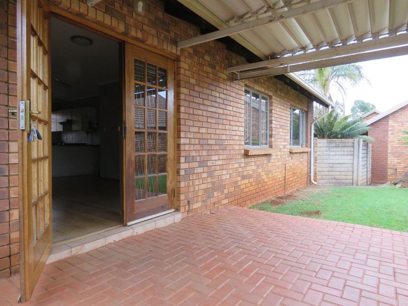 A covered patio area featuring brick paving and facebrick exterior walls, providing direct access to the interior through timber-framed glass doors.