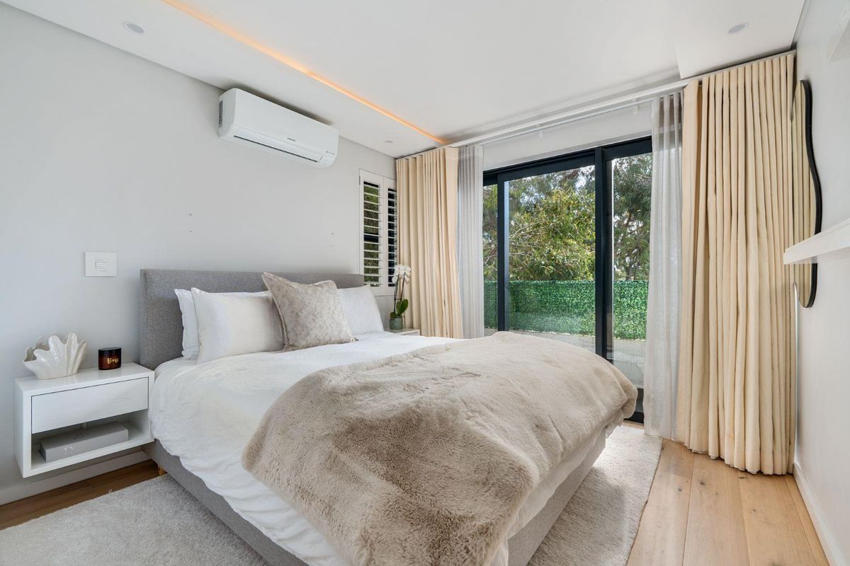 Modern bedroom featuring timber flooring, recessed ceiling lighting, split-system air conditioning, and large sliding glass doors opening to an outdoor area.