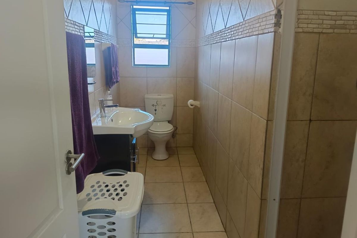 A functional bathroom featuring ceramic wall and floor tiling, a pedestal washbasin, toilet, and a shower enclosure with a top-hung window for ventilation.