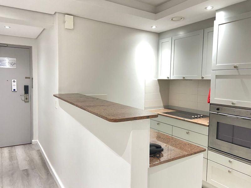 A compact, well-maintained kitchen featuring light-toned cabinetry, granite countertops, a built-in oven, and an electric hob with an integrated breakfast bar.