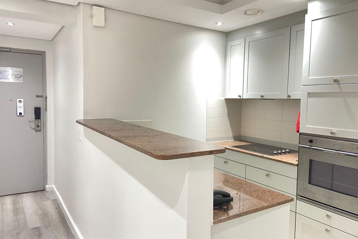 A compact, well-maintained kitchen featuring light-toned cabinetry, granite countertops, a built-in oven, and an electric hob with an integrated breakfast bar.