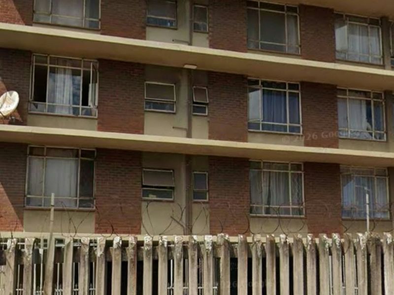 Exterior view of a multi-story apartment building featuring a brick facade, concrete balconies, and security fencing with razor wire.