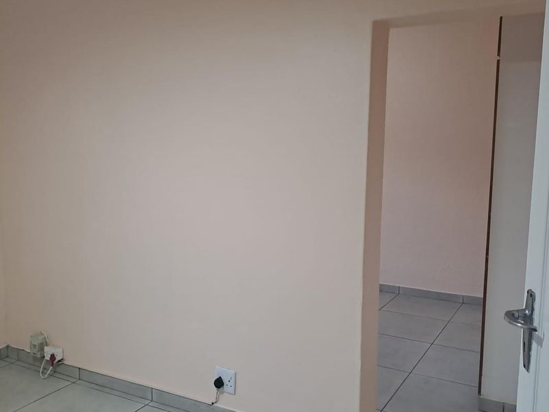 An empty bedroom featuring neutral painted walls, tiled flooring, and a doorway leading to an adjacent space.