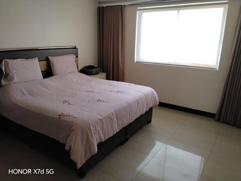 A well-lit bedroom featuring neutral tiled flooring and fitted curtain tracks, providing a clean and functional space.