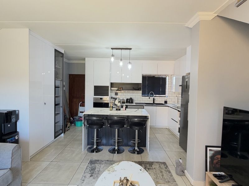 Modern open-plan living area featuring a contemporary kitchen with a central island, stone countertops, built-in appliances, and sleek white cabinetry.