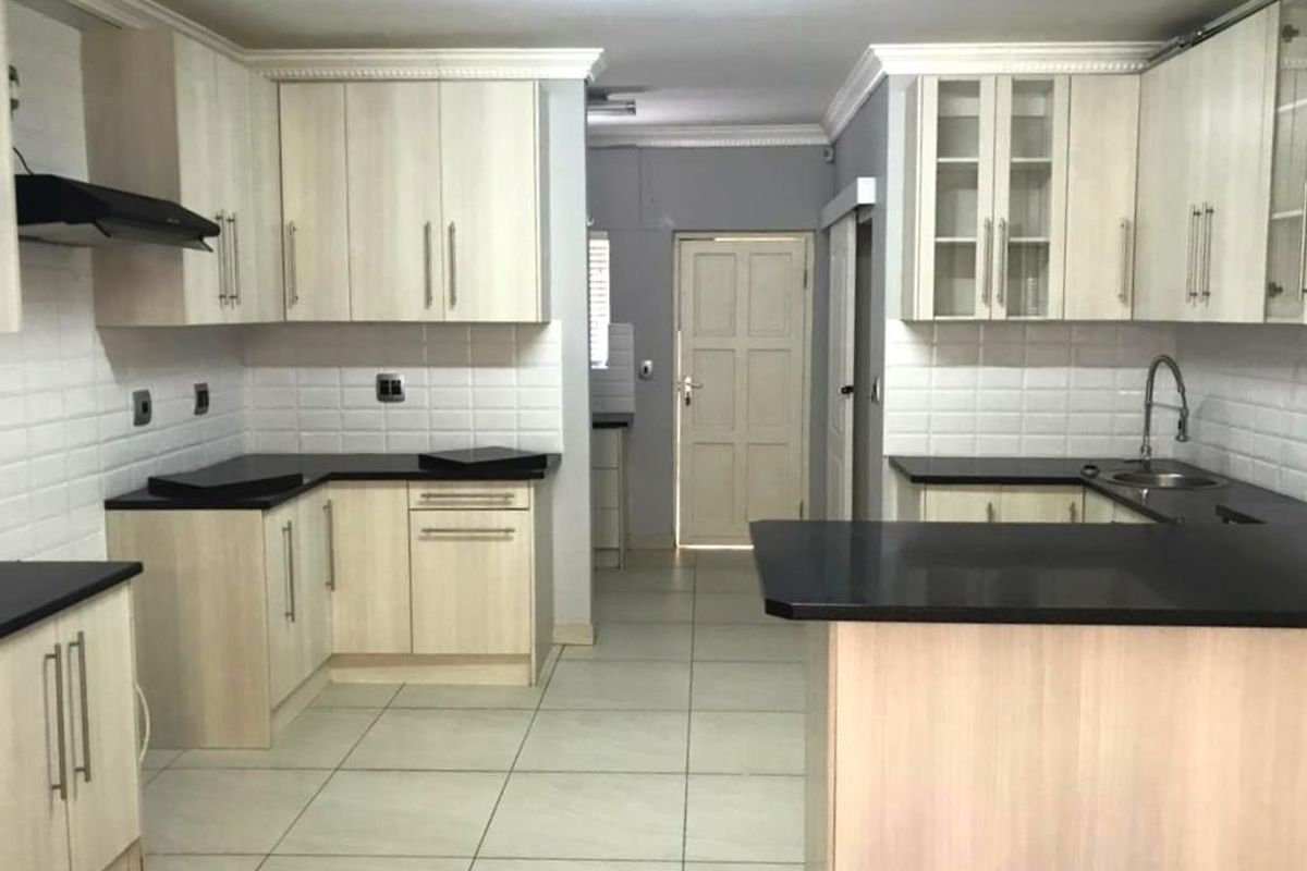 A spacious, well-lit kitchen featuring light wood cabinetry, contrasting black countertops, subway tile backsplash, and neutral floor tiles.