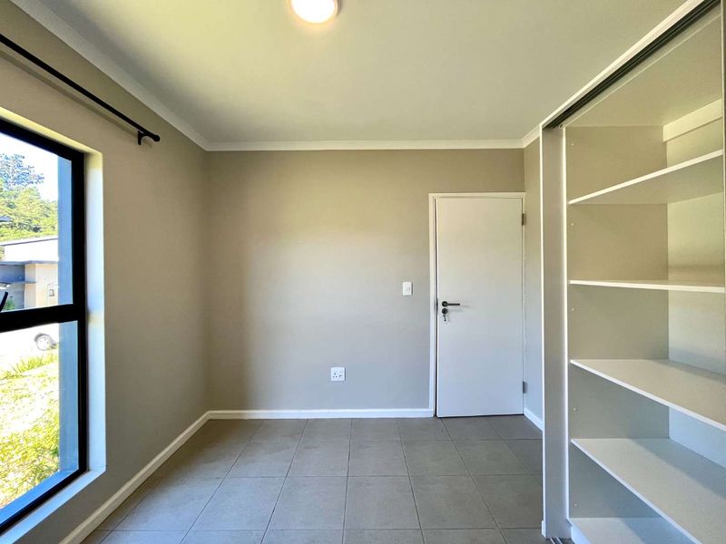 A bright, empty bedroom featuring neutral wall tones, tiled flooring, and built-in shelving units, offering a clean and versatile space.