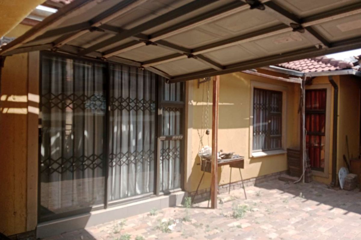Rear exterior area featuring a paved patio space, sliding glass doors with security gates, and a partially covered structure.