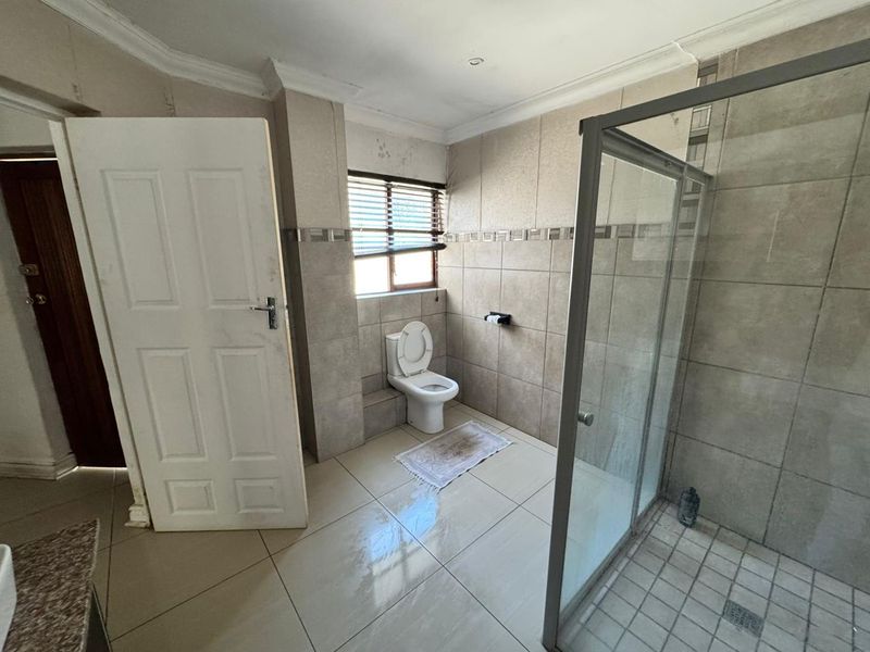 A functional bathroom featuring a glass-enclosed shower, tiled walls and flooring, and a standard toilet, offering a neutral base for potential cosmetic updates.