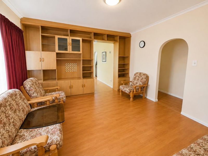 A living room featuring laminate flooring, a large built-in wooden shelving unit, and an arched doorway leading to an adjacent space.