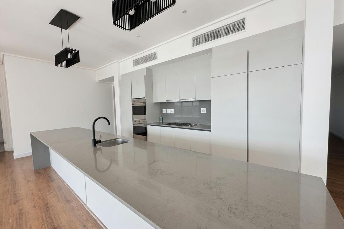 Modern open-plan kitchen featuring a large stone-topped island, integrated cabinetry, built-in oven, gas hob, and sleek black fixtures.