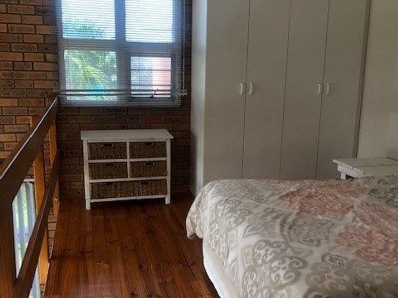 Bedroom featuring exposed brick walls, timber flooring, built-in wardrobes, and a ceiling fan, overlooking a lower level via a timber balustrade.