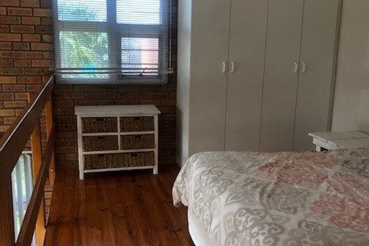 Bedroom featuring exposed brick walls, timber flooring, built-in wardrobes, and a ceiling fan, overlooking a lower level via a timber balustrade.