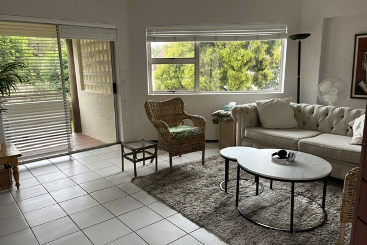 Bright living room featuring tiled flooring, large windows with venetian blinds, and a sliding glass door providing access to an outdoor patio area.