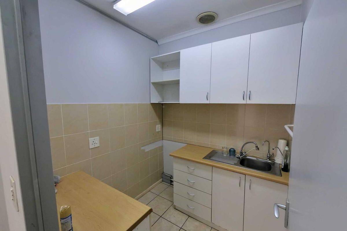 A functional office kitchenette featuring white cabinetry, a stainless steel sink, tiled splashbacks, and laminate countertops.