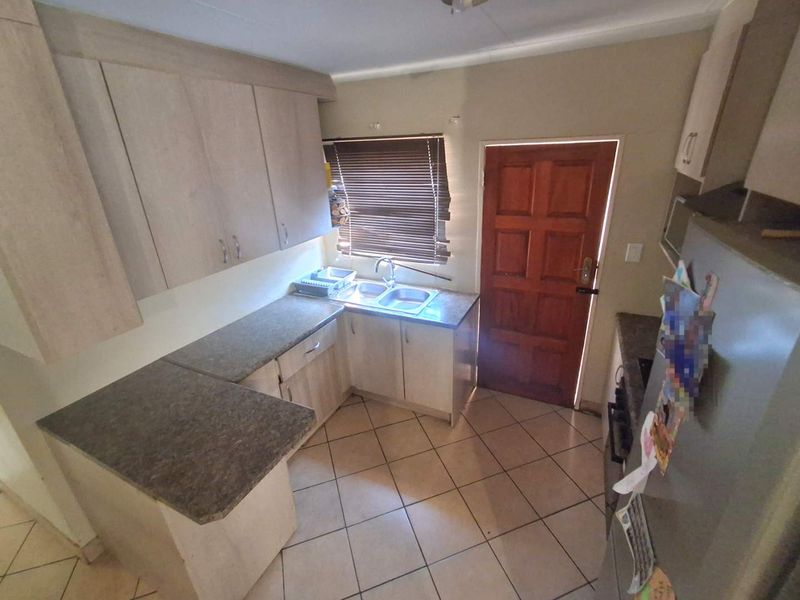 A functional kitchen featuring laminate cabinetry, stone-look countertops, a double bowl sink, and ceramic floor tiles with direct access to an exterior door.