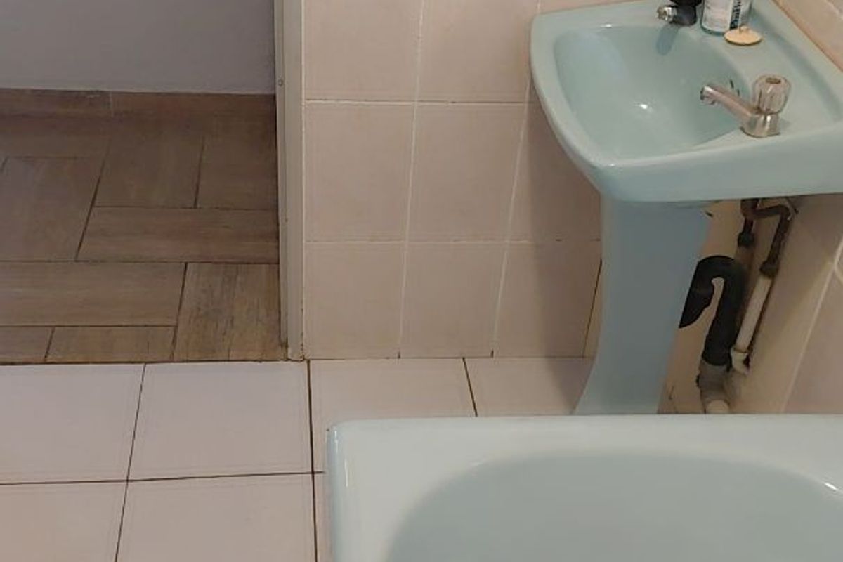 A dated bathroom featuring a pastel blue pedestal basin and matching bathtub with exposed plumbing and neutral wall tiling.