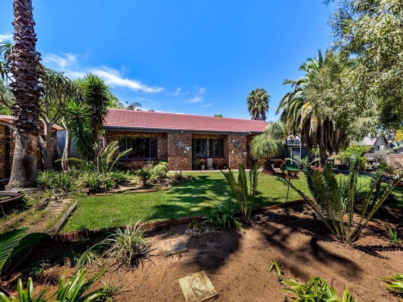 A well-maintained rear exterior view of a face brick house featuring a tiled roof and a spacious, landscaped garden with mature trees.