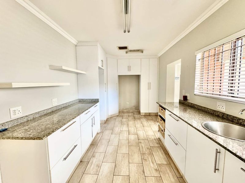 A clean, modern kitchen featuring white cabinetry, granite countertops, tiled flooring, and ample storage space, presented in a bright and well-maintained condition.