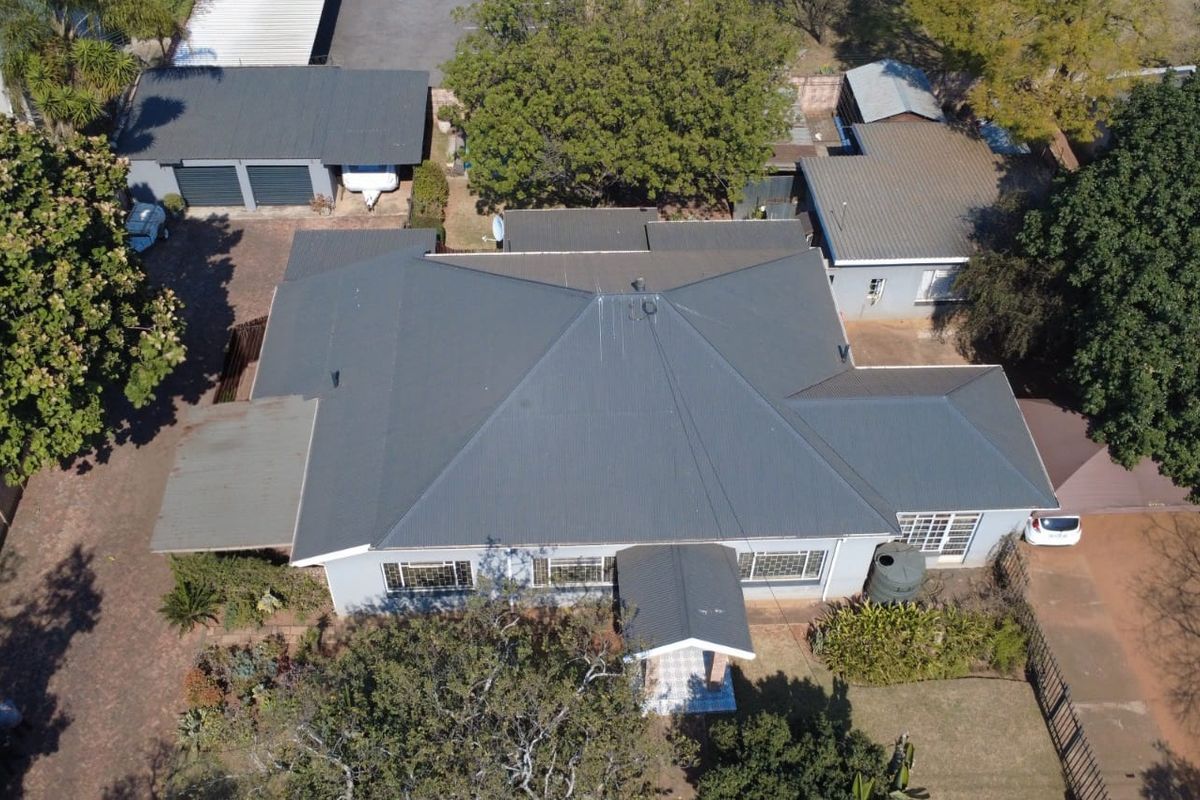 Aerial view of the property showing the main house with a corrugated metal roof, detached garage, and surrounding garden area.
