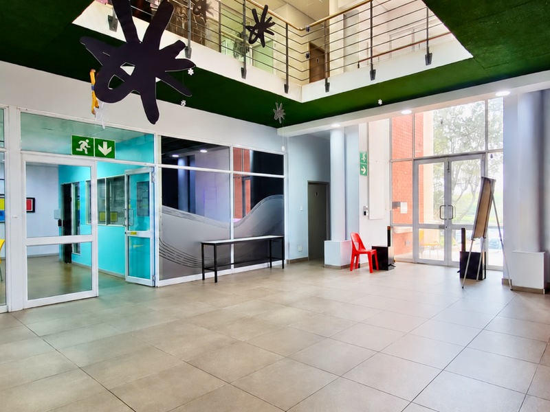 Spacious office lobby area featuring tiled flooring, glass partitions, and a mezzanine level with a modern metal balustrade, providing an open and bright workspace.