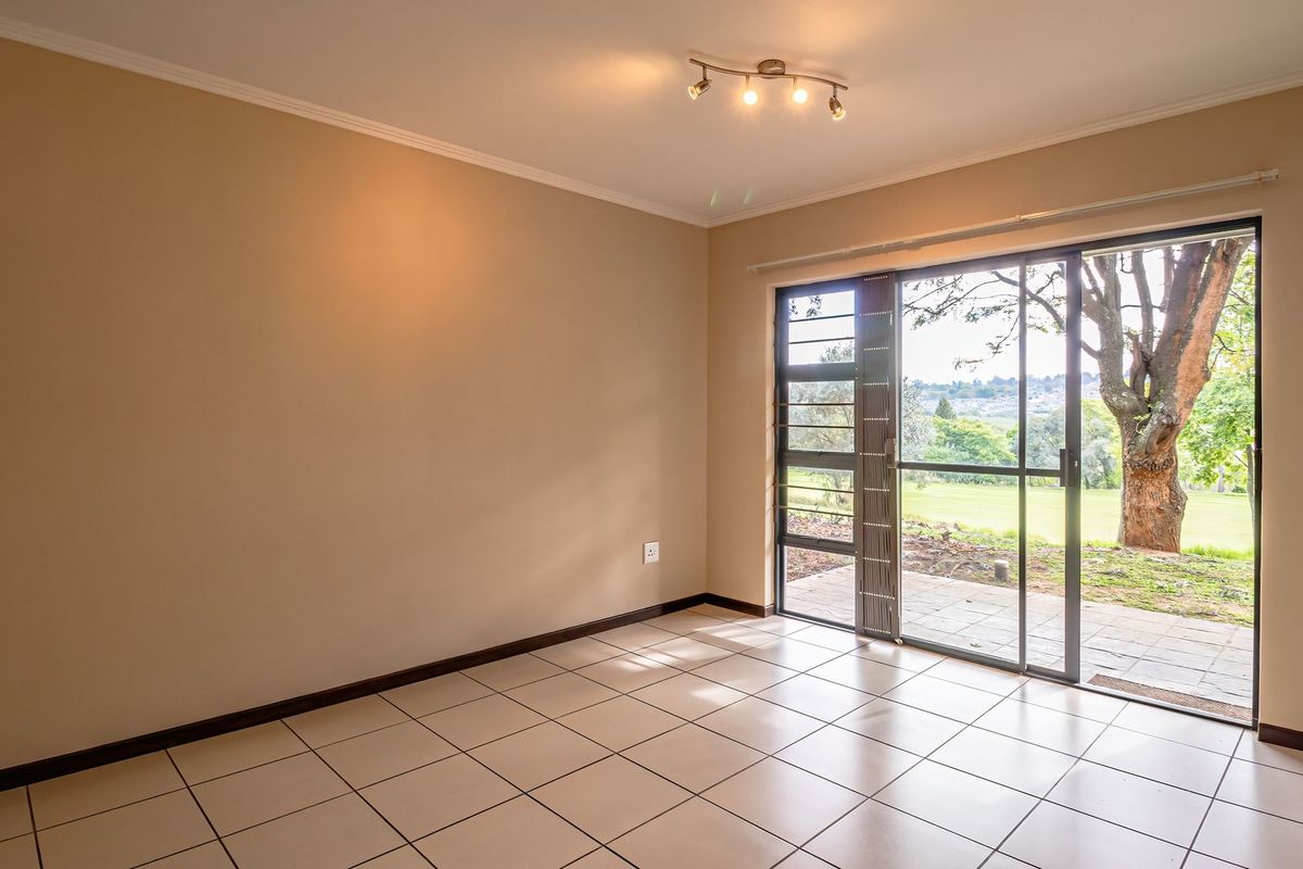 A bright, empty living room featuring neutral walls, tiled flooring, and a large sliding glass door providing direct access to the outdoor patio and garden.