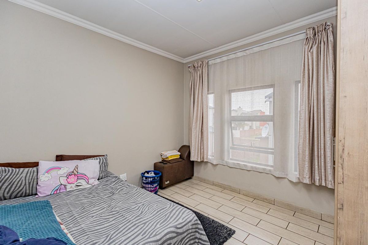 A bedroom featuring tiled flooring, a built-in wardrobe, and a large window with curtain tracks, providing a functional and well-lit living space.