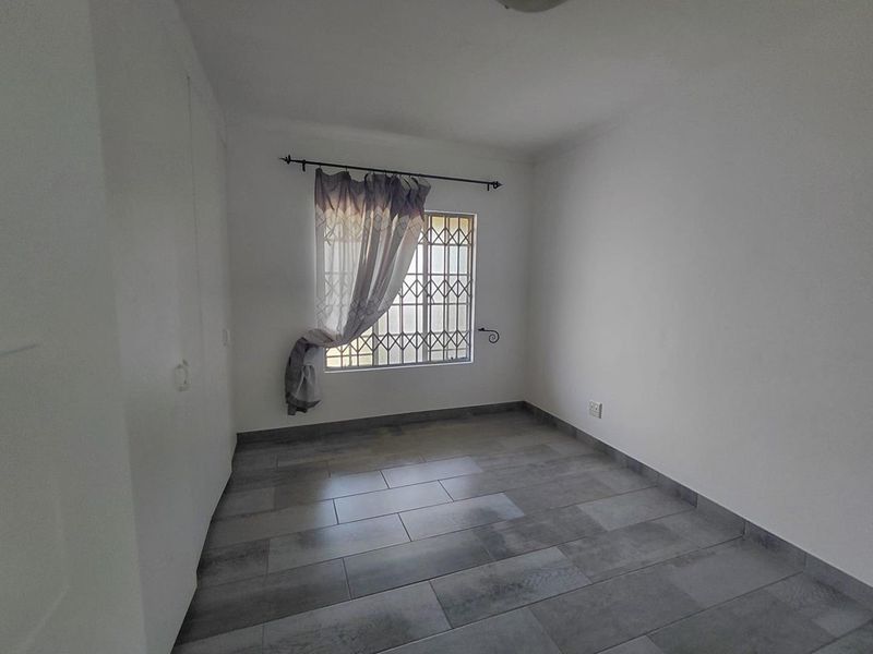A clean, empty bedroom featuring modern grey tiled flooring, built-in cupboards, and a window fitted with a security gate.