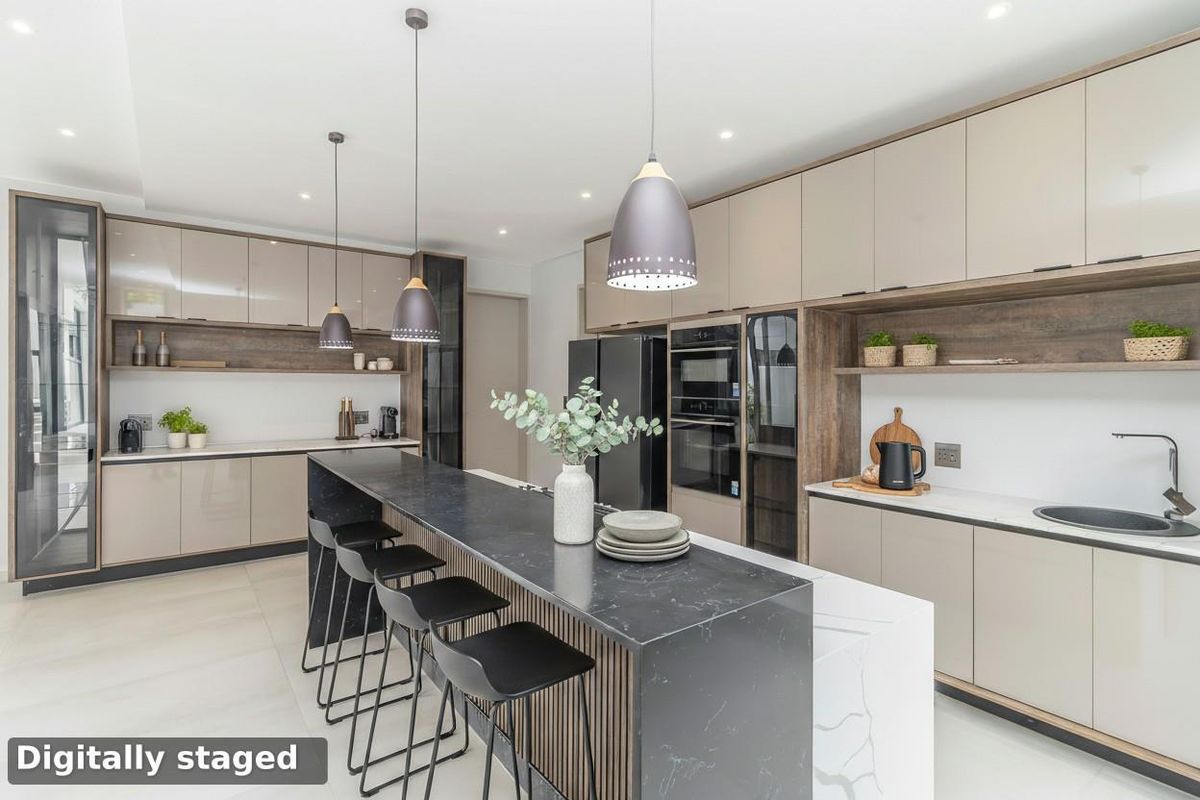 Modern kitchen featuring sleek cabinetry, a large stone-topped island with breakfast bar seating, integrated ovens, and contemporary pendant lighting.
