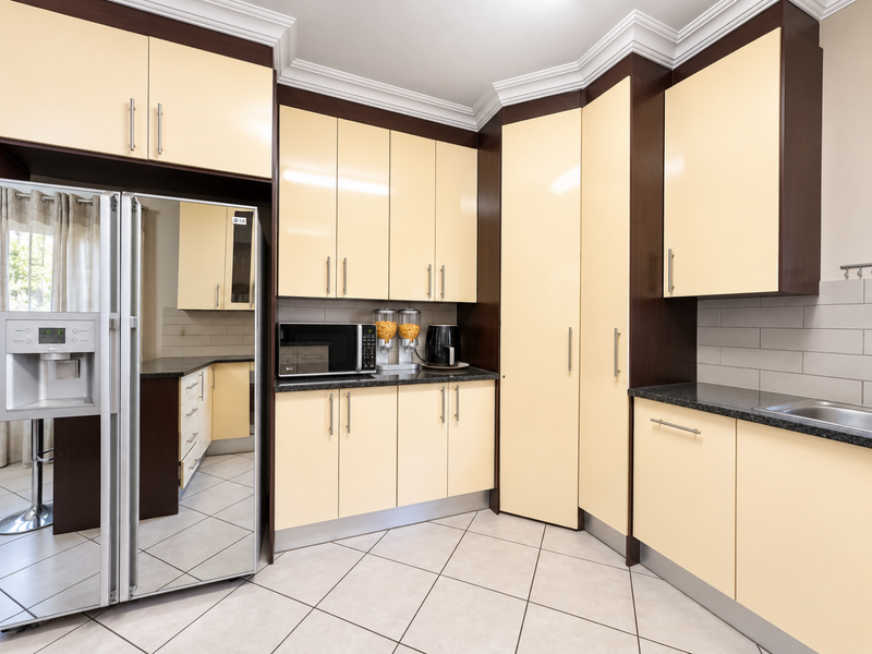 A well-maintained kitchen featuring cream-colored cabinetry, dark granite countertops, stainless steel sink, and tiled flooring with ample storage space.