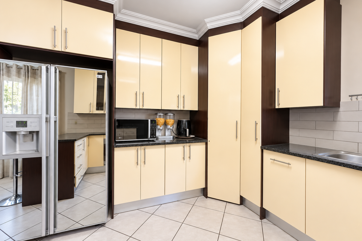 A well-maintained kitchen featuring cream-colored cabinetry, dark granite countertops, stainless steel sink, and tiled flooring with ample storage space.