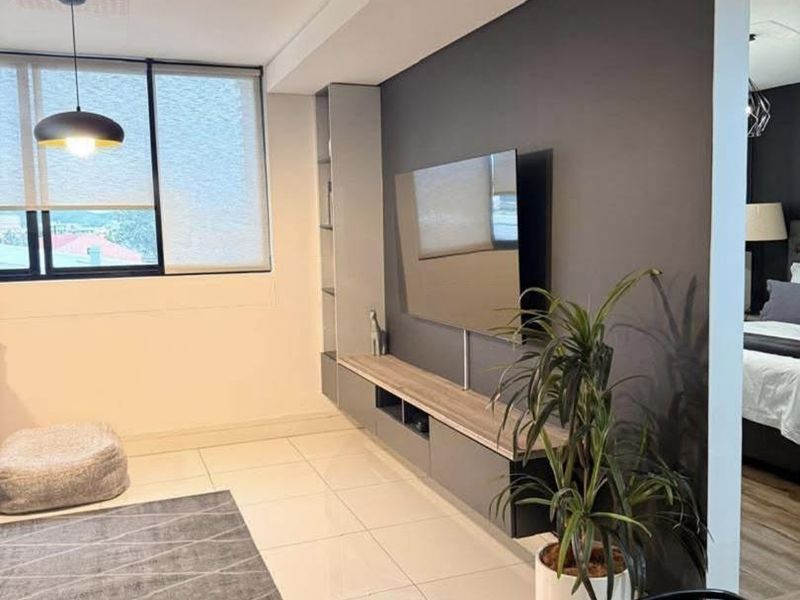 Modern living room featuring sleek tiled flooring, a custom built-in media console, and recessed ceiling lighting with large windows providing natural light.