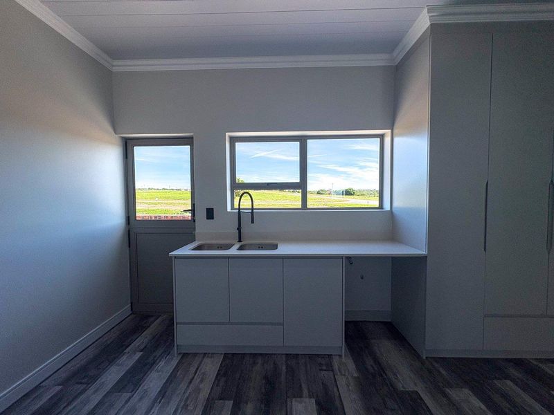 A clean, modern scullery featuring built-in cabinetry, a double sink with a gooseneck faucet, and direct access to the exterior.