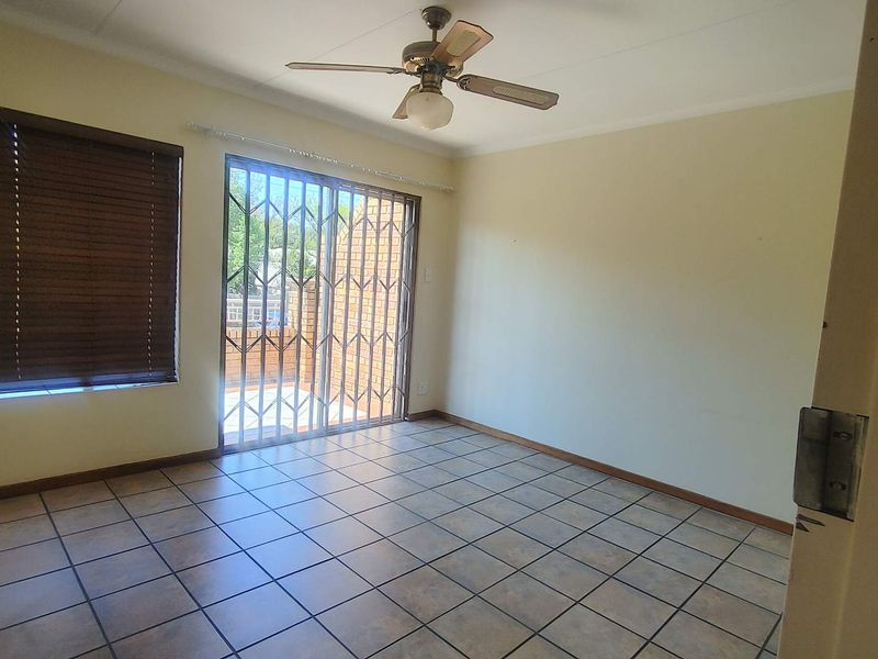 An empty living room featuring tiled flooring, a ceiling fan, and a security gate leading to an outdoor area.