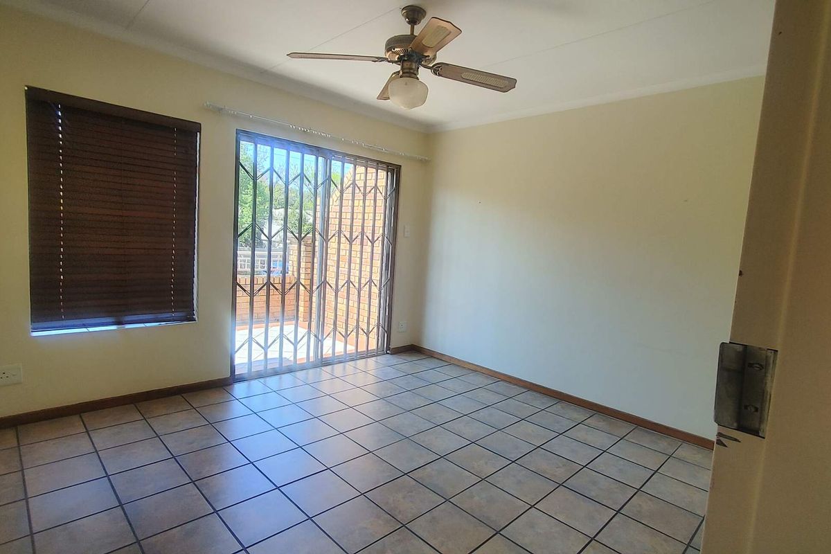 An empty living room featuring tiled flooring, a ceiling fan, and a security gate leading to an outdoor area.