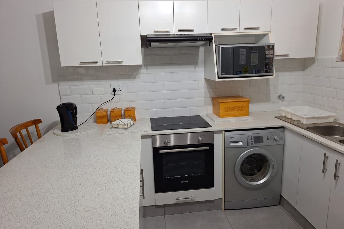 Modern kitchen featuring white cabinetry, subway tile backsplash, stone countertops, built-in oven, electric hob, extractor fan, and an integrated washing machine.
