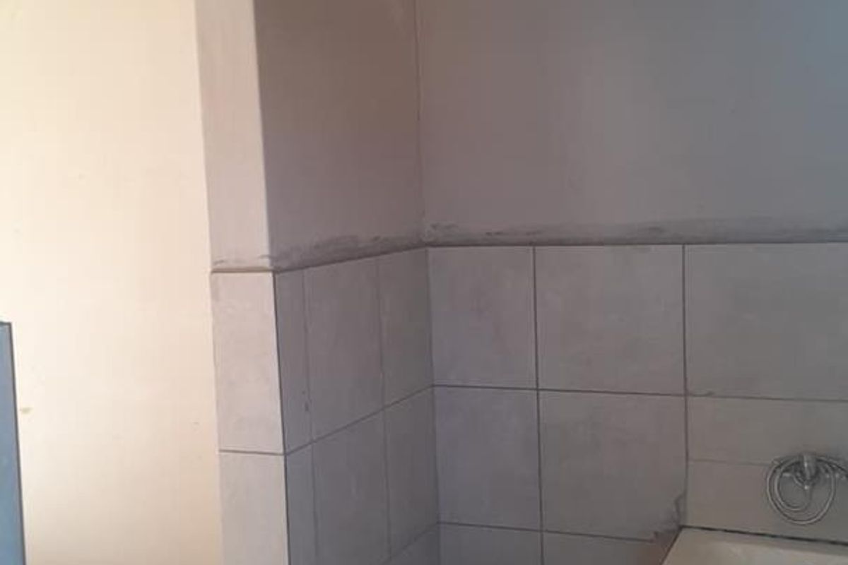 A bathroom in the process of renovation, featuring a built-in bathtub and partially tiled walls, requiring finishing touches to complete the space.