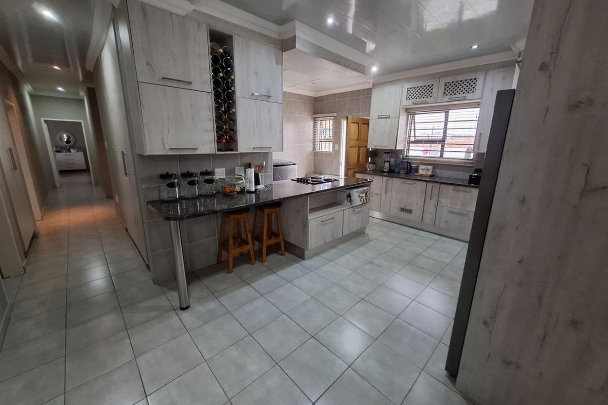 Modern kitchen featuring light wood-grain cabinetry, granite countertops, a breakfast bar, built-in wine storage, and tiled flooring with recessed lighting.