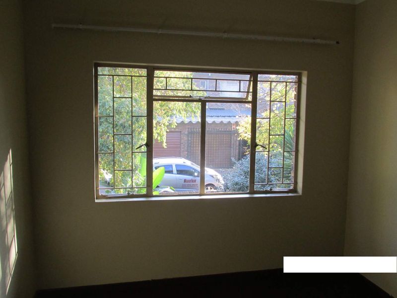 An empty bedroom featuring a large window with integrated metal security burglar bars and a mounted curtain rail.