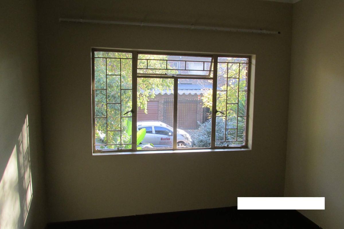 An empty bedroom featuring a large window with integrated metal security burglar bars and a mounted curtain rail.