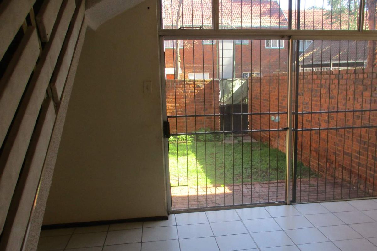 An empty living area featuring tiled flooring and a sliding glass door with security gate, providing direct access to a private rear garden.
