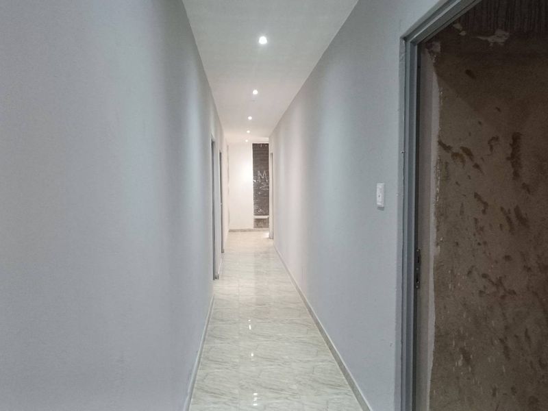 A long, empty hallway featuring tiled flooring and recessed downlighting, currently showing unfinished wall and door frame sections requiring completion.