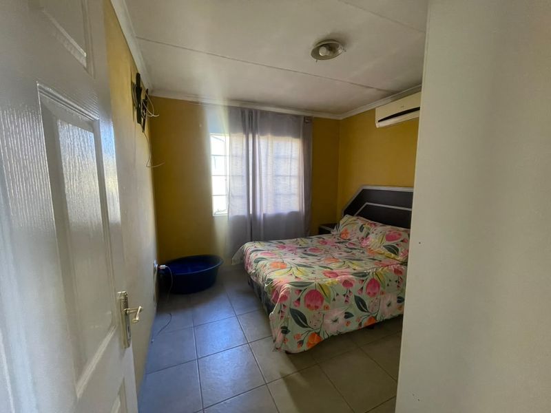 A compact bedroom featuring tiled flooring, an air conditioning unit, and a window, requiring cosmetic updates to improve its overall appeal.