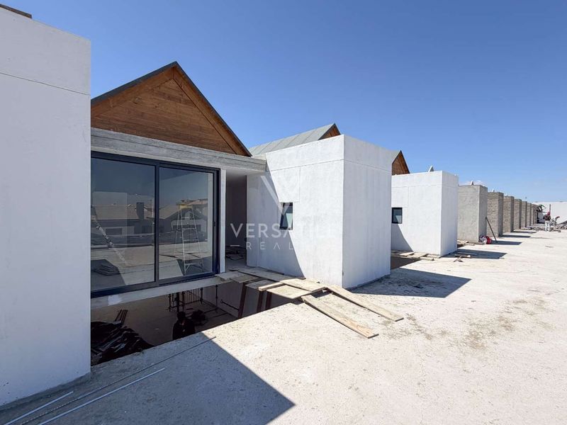 Rear view of a townhouse development under construction, featuring modern architectural lines, sliding glass doors, and unfinished concrete terrace areas.