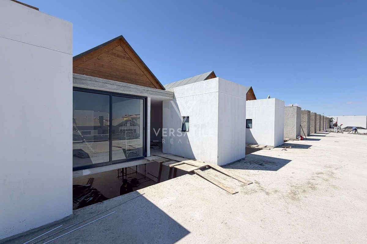 Rear view of a townhouse development under construction, featuring modern architectural lines, sliding glass doors, and unfinished concrete terrace areas.