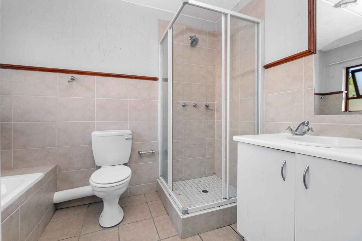 A functional bathroom featuring a shower enclosure, a vanity with a basin, and a toilet with an exposed waste pipe.
