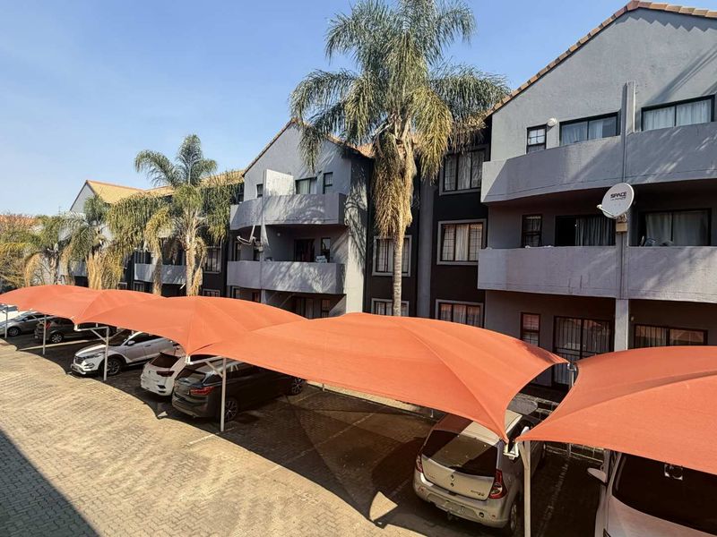 Exterior view of an apartment complex featuring multi-story residential units with private balconies and dedicated shade cloth covered parking bays.