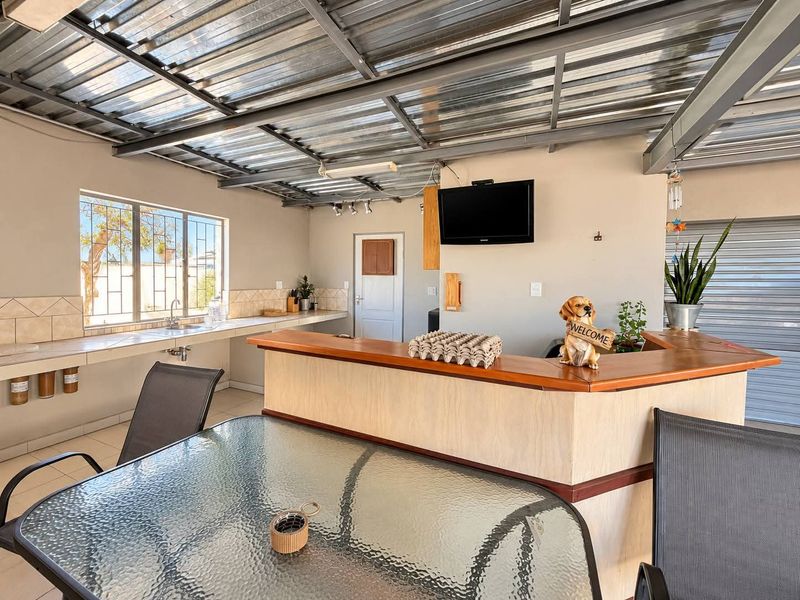 Covered outdoor entertainment area featuring a built-in bar, tiled prep counter with sink, and secure roller shutter access.