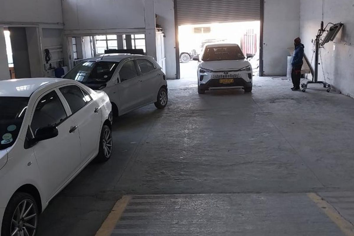 Spacious industrial garage featuring high ceilings with exposed timber trusses, concrete flooring, and a large roller shutter door for vehicle access.