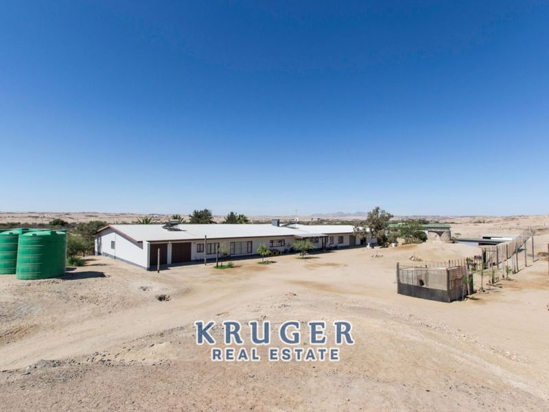 Aerial view of a small holding property featuring a main dwelling, large water storage tanks, and expansive surrounding land in an arid landscape.